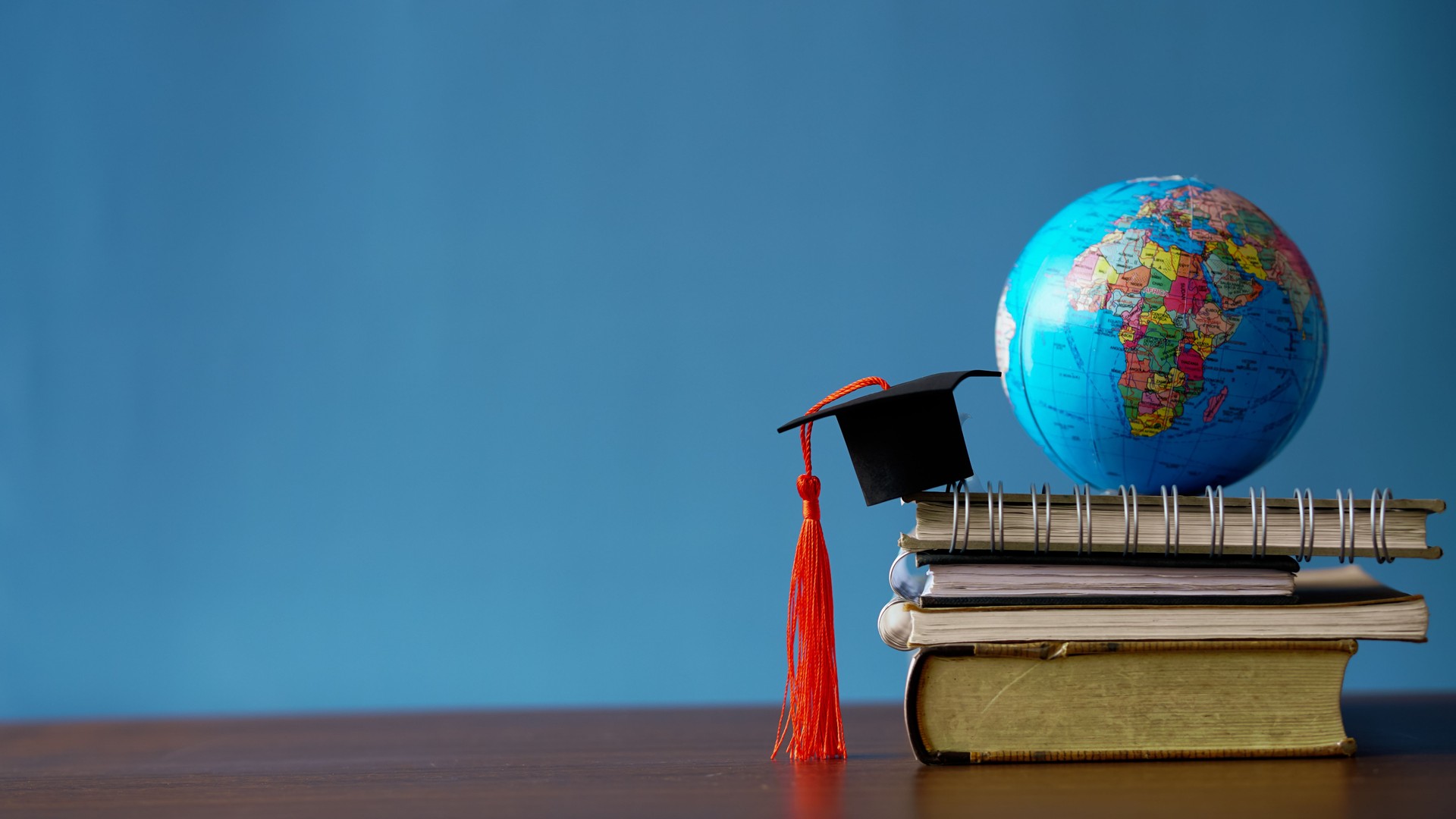 A symbolic representation of global education, academic success, and knowledge — featuring graduation cap, books, globe, and diploma on a blue background.