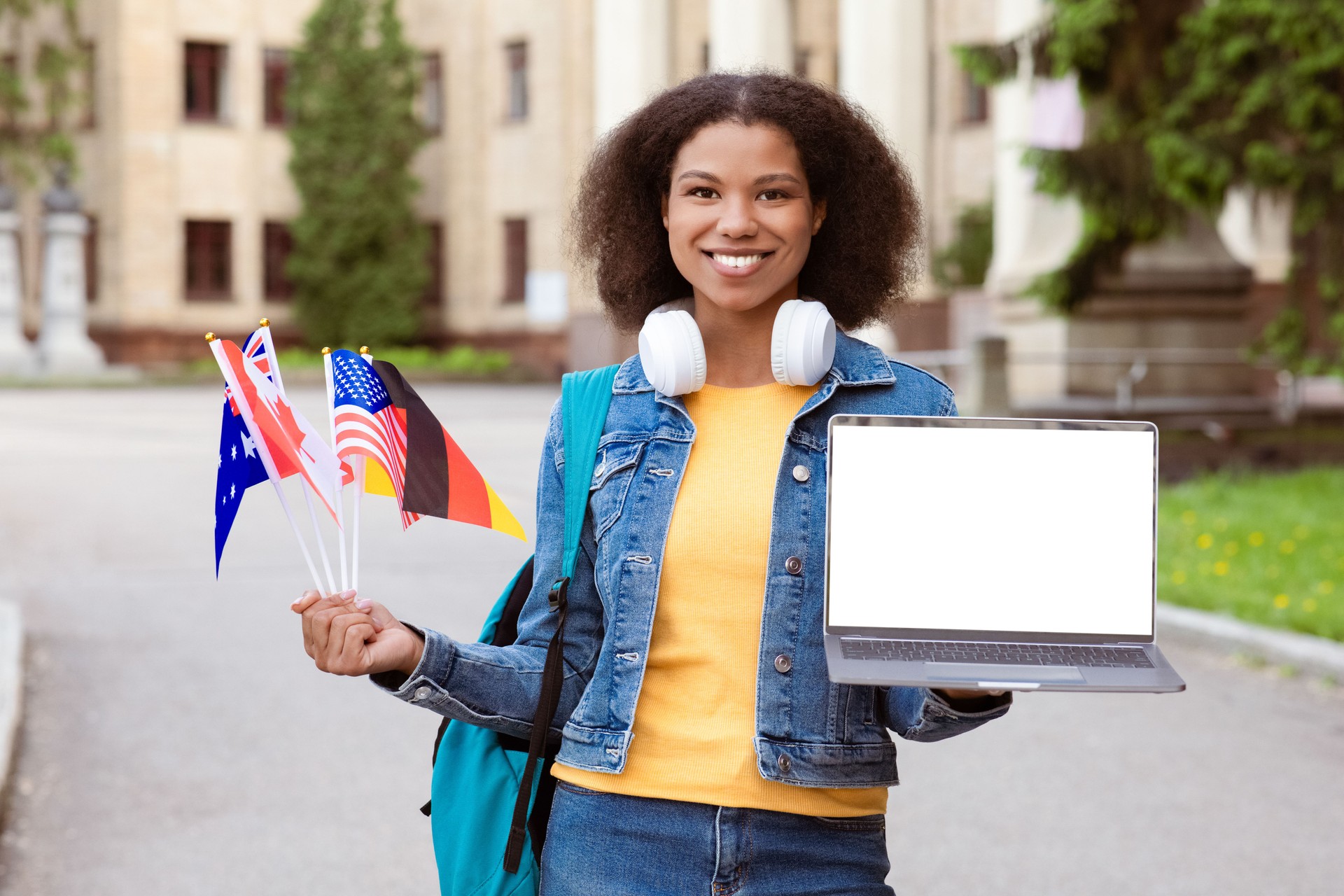 Black female student outdoors holding international flags and laptop with blank screen